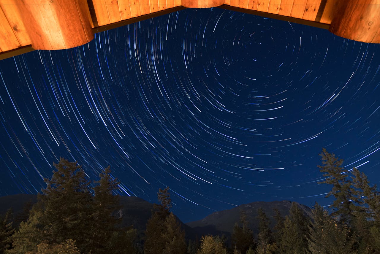 creative-03 Stunning star trails forming circles above a serene forest view framed by a wooden cabin roof.