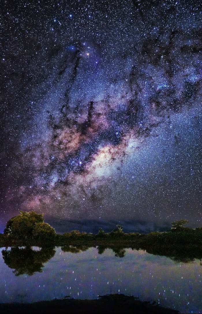 mobile-02 A breathtaking view of the Milky Way galaxy reflecting on a serene lake surrounded by nature.